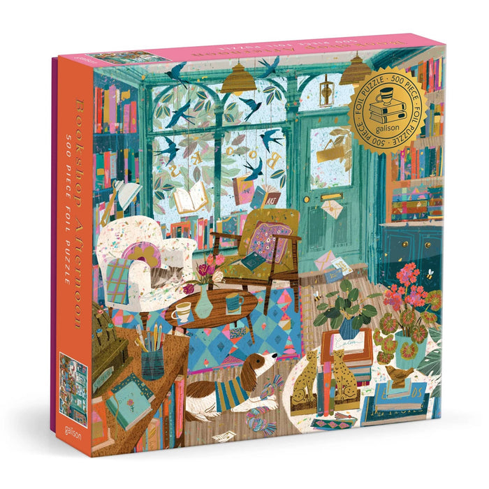 A boxed jigsaw puzzle package shown at a slight angle on a white background. The box art depicts a cozy, detailed bookshop interior scene with teal window frames, bookshelves, chairs, plants, flowers, and a dog.