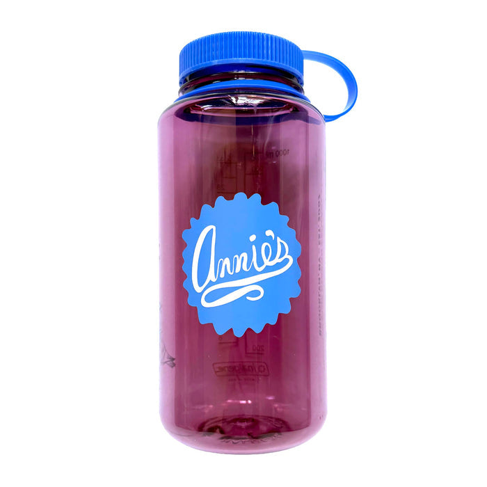 Pink clear Nalgene water bottle with the Annie's seal in blue and a blue screw-top lid, front view, on a white background.