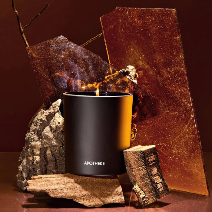 Black Apotheke candle with wooden elements and amber on a dark background.
