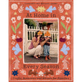 The front cover of the book 'At Home in Every Season' by Courtney and Michael Adamo. The cover features a terracotta orange background decorated with whimsical folk-art illustrations of bunnies, birds, flowers, and stars, surrounding a central color photograph of a woman and child wearing orange paper hats.