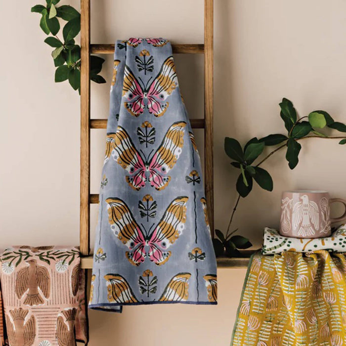 Butterfly patterned towel hanging on a wooden ladder with plants and a mug in the background.