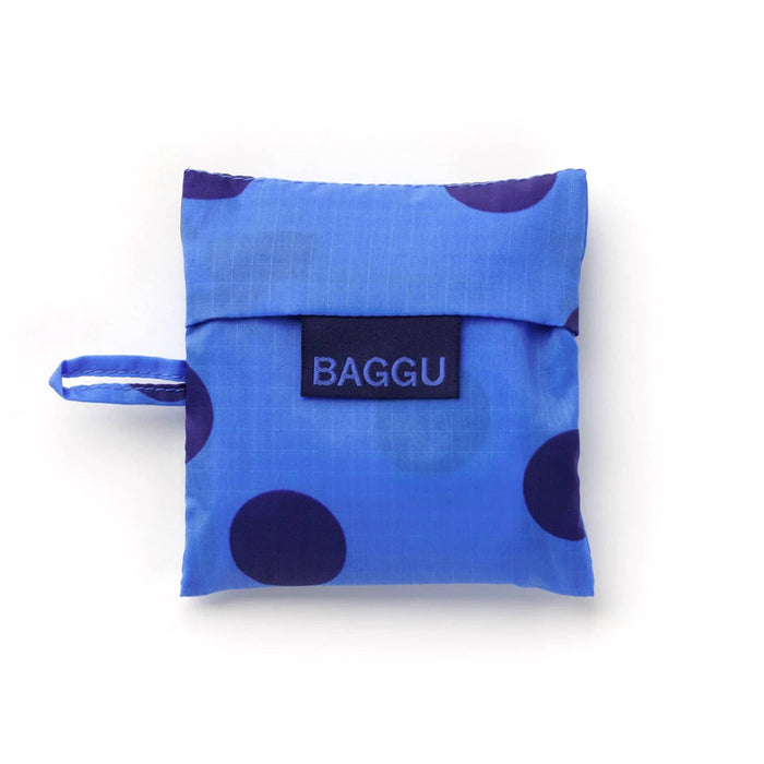 A blue reusable bag in matching pouch with dark blue polka dots and a navy brand label reading 'BAGGU' on a white background.