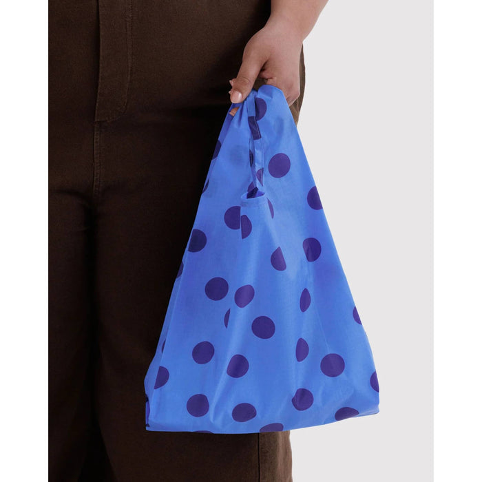 A person holding a reusable ripstop nylon shopping bag with a blue base and dark blue polka dots, shown against a plain light gray background.