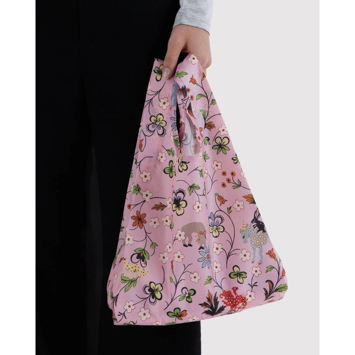 A person holds a pink reusable tote bag with a colorful floral pattern against a light gray background.