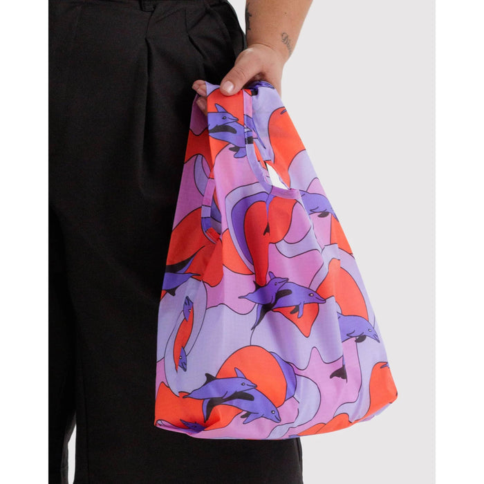 Person holding a colorful bag with dolphin pattern against a white background.