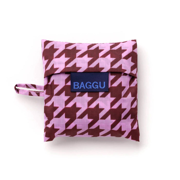 A small zippered pouch with a pink and dark red houndstooth pattern, featuring a navy blue brand label that reads 'BAGGU' in light blue text. A matching houndstooth loop is attached to the left side.