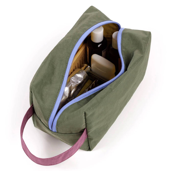 A caper green toiletry bag with a plum handle and light blue zipper, shown open with various toiletry bottles and containers inside, on a white background.