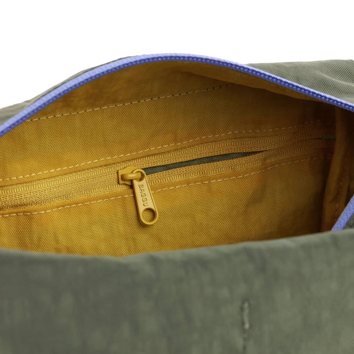 Close-up of the interior of a bag showing a mustard yellow fabric lining with a matching zipper pocket and a gold-tone zipper pull engraved with 'BAGGU'.