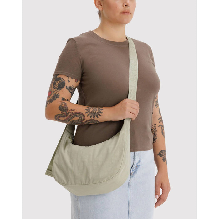 Person wearing a brown shirt and light blue jeans with a green shoulder bag on a white background.