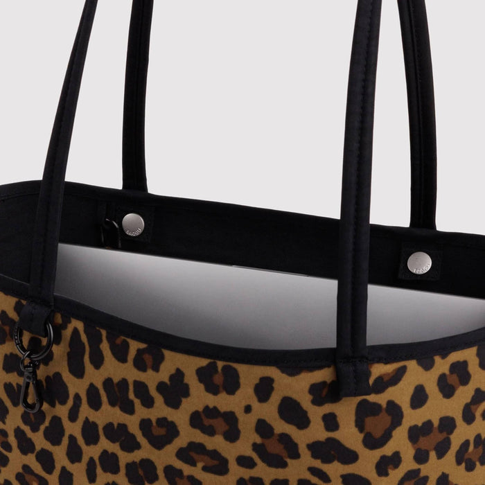 Close-up of a leopard print tote bag with black handles and a black top trim, shown against a light gray background.