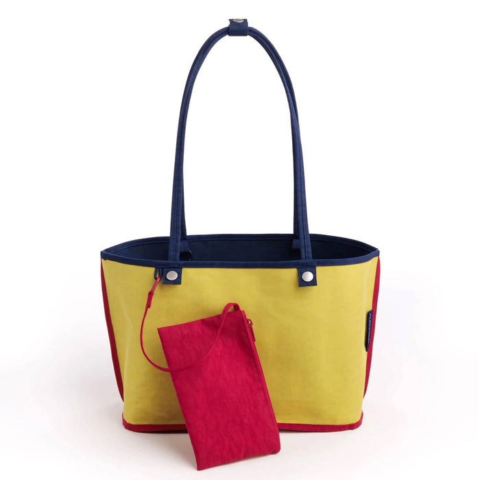 A yellow canvas tote bag with navy blue handles and trim and interior, shown with a small matching red pouch in front, on a plain white background.