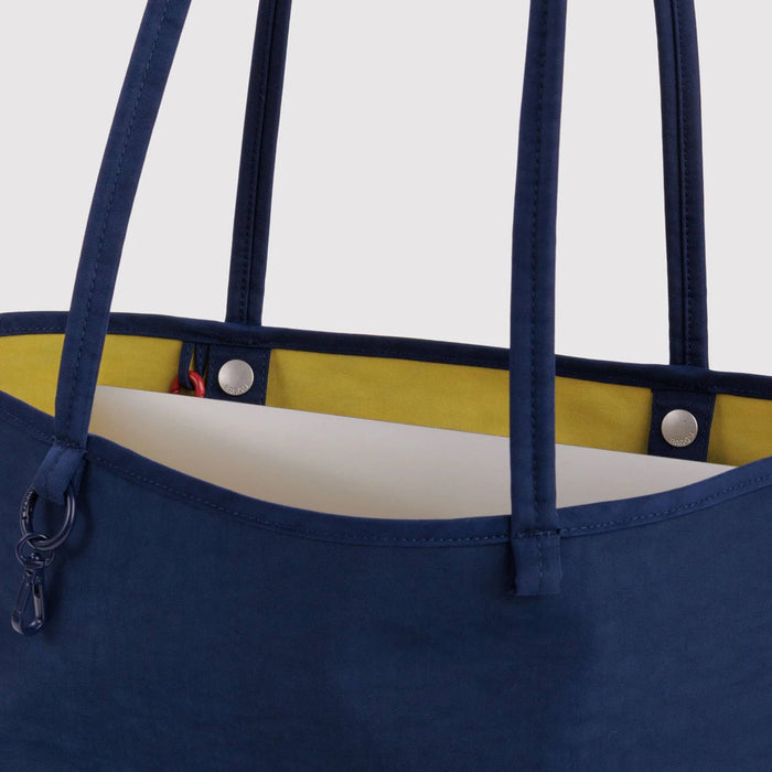 Close-up of a navy blue tote bag with a bright yellow interior lining and silver snap hardware, shown against a light gray background.