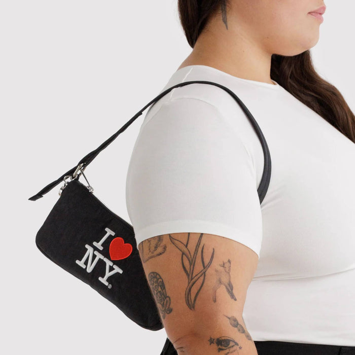Person with a small black nylon shoulder bag with 'I ❤️ NY' text on a plain background.