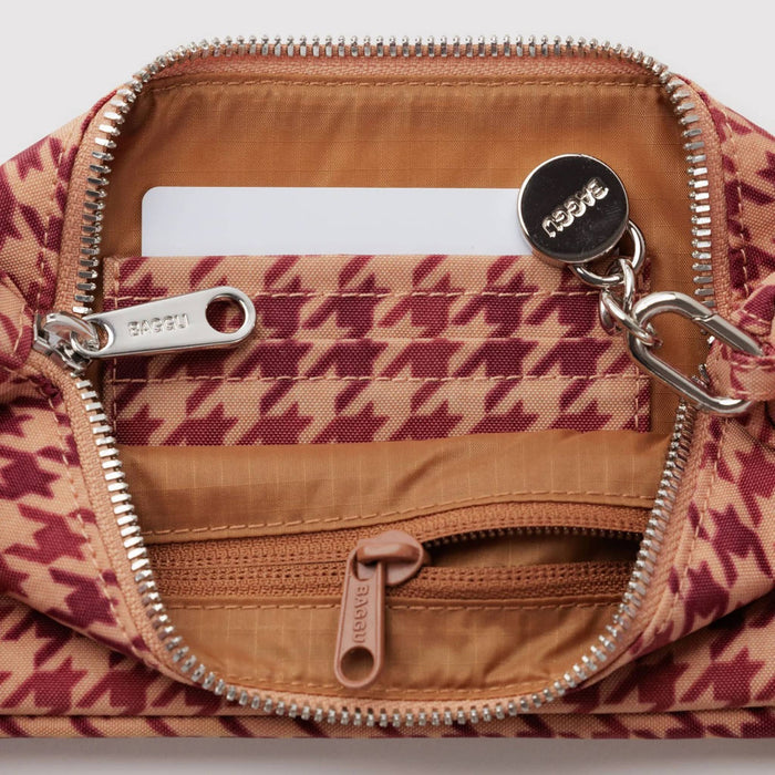 Close-up of a patterned bag interior with silver zippers, a tan lining, and a round silver brand tag reading BAGGU.