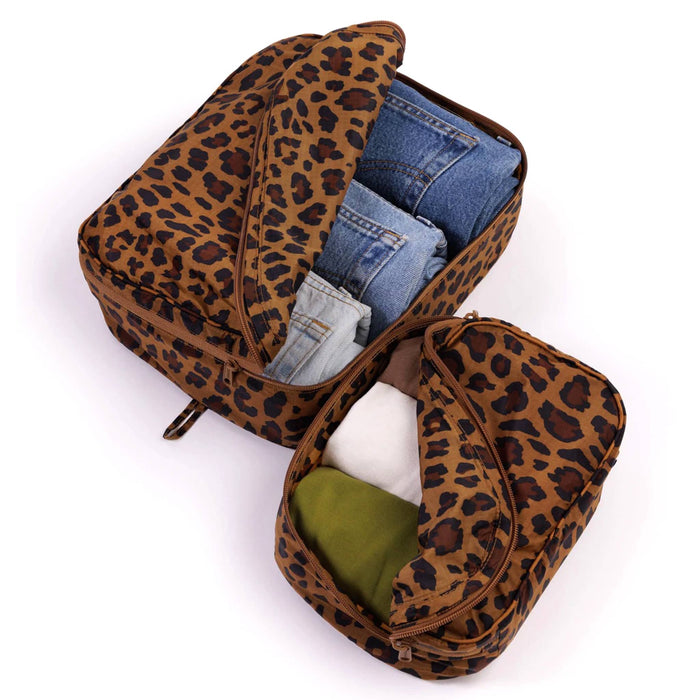 Leopard print travel bags with denim jeans and t-shirts inside, on a white background.