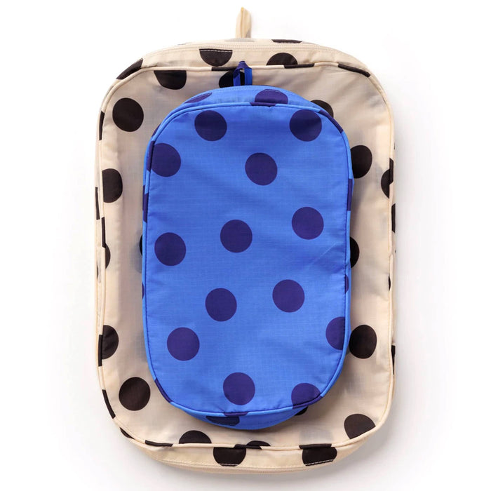 2 recycled nylon zippered packing cubes, large bag is cream with black polka dots, smaller bag is blue with navy polka dots, stacked flat on a white background.