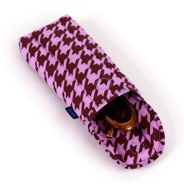 A pink and brown quilted fabric glasses pouch with a houndstooth pattern, featuring a fold-over flap and a small dark blue brand tag on the side, lying down and open with sunglasses inside on a white background.
