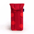A red quilted fabric glasses pouch with a large polka dot pattern in shades of red, featuring a fold-over flap and a small dark blue brand tag on the side.