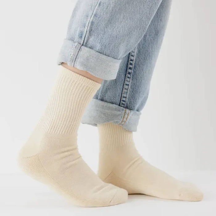 Ribbed ecru socks worn with rolled-up blue jeans on a light gray background.