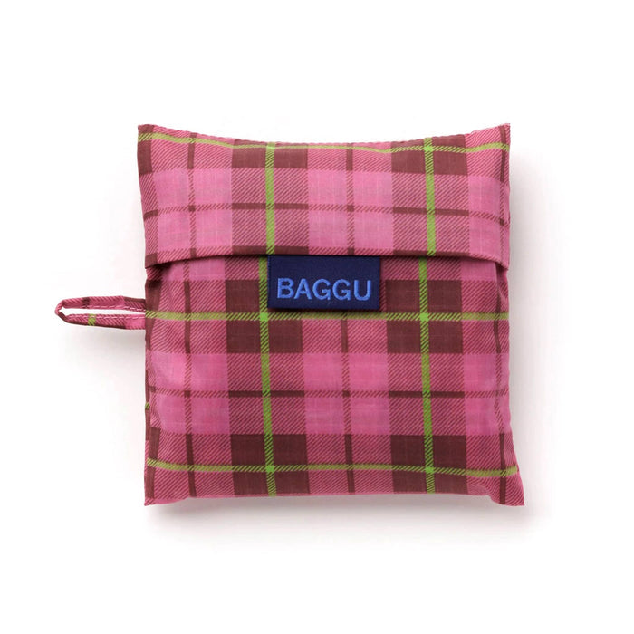 A pink and lime green tartan reusable bag folded in a matching pouch with a blue brand label that reads 'BAGGU' and a small side loop, shown on a white background.