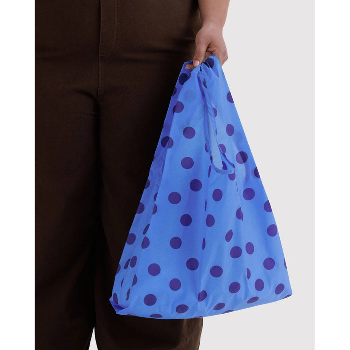 A person holding a reusable blue shopping bag with dark blue polka dots, shown against a plain light gray background.