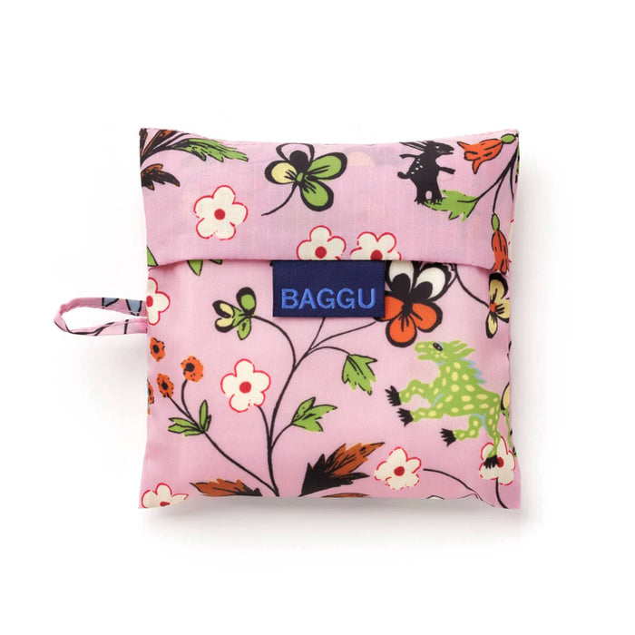 A folded reusable bag from BAGGU in a pink pouch with floral and mythical creatures print, featuring a blue BAGGU brand label on the front and a small carrying loop on the left side, photographed on a white background.