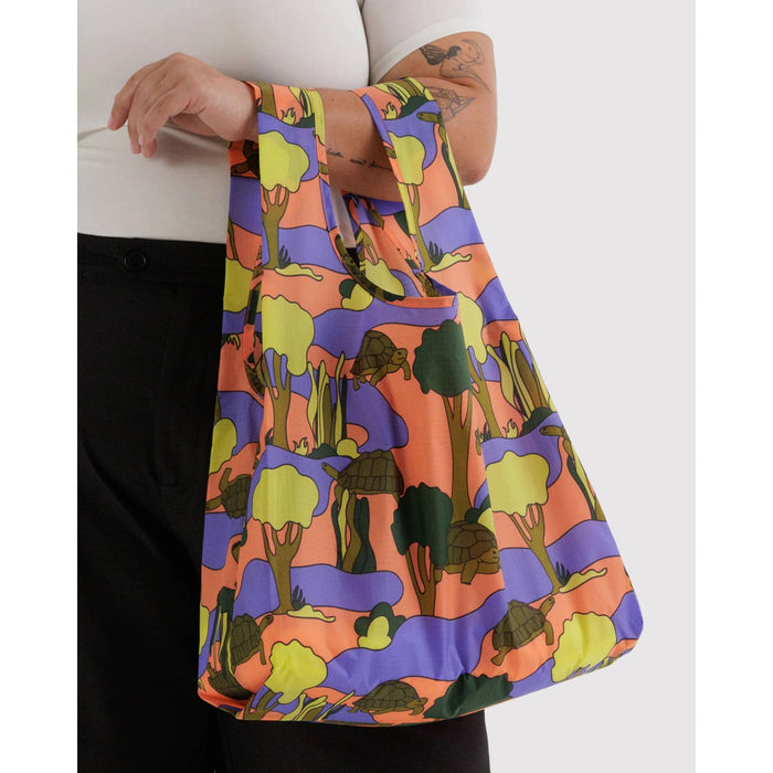 Colorful bag with a turtle pattern held by a person against a white background.