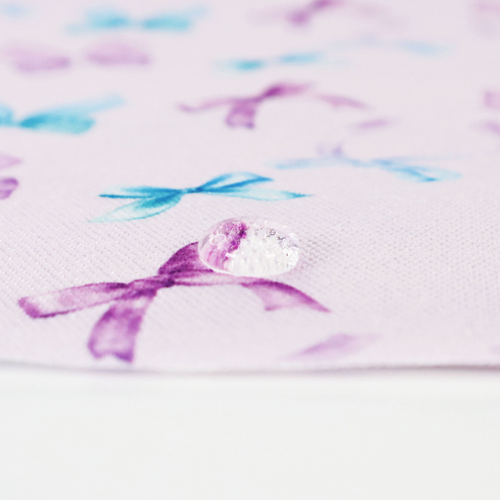 This printed WPC-Lite consists of a variety of styled bows in blue, turquoise, purple, and magenta. This photo shows a water drop on the fabric.