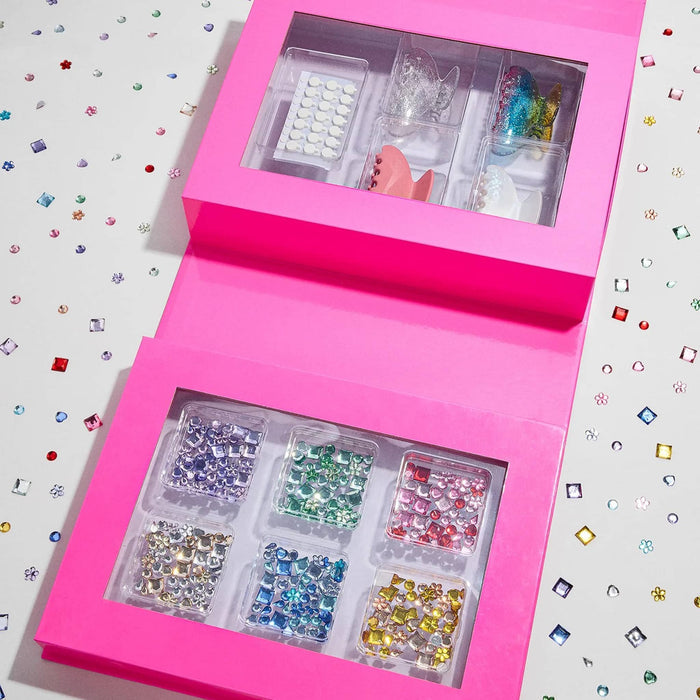 Hair claw making kit, pink box open showing contents in packaging on a white background with gems scattered.