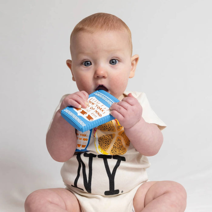 Baby chewing on a natural rubber baby teether toy that looks like a greek coffee cup, on a gray background.