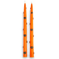 A pair of tall orange taper candles decorated with small black cat faces, shown on a plain white background.