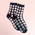 Sheer black and white grid patterned socks on a light pink background.