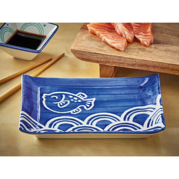 Blue ceramic plate with fish design on a wooden table with salmon and soy sauce.