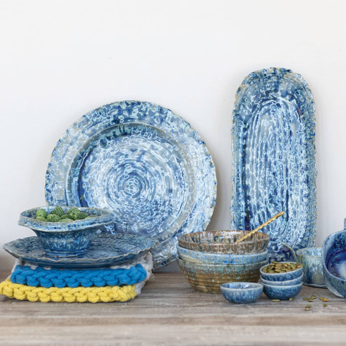 Various stoneware serving pieces with a blue crackle finish glaze on a wood surface.