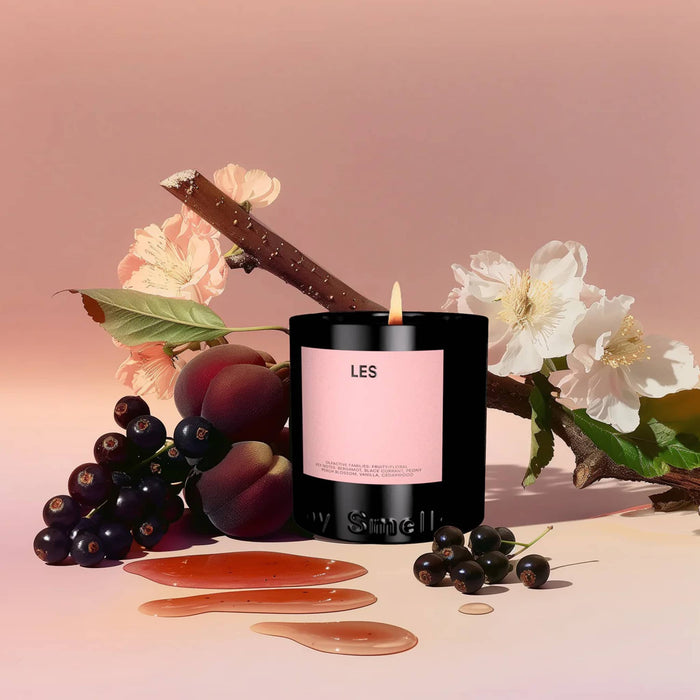 Candle with a pink label surrounded by fruits and flowers on a soft pink background.