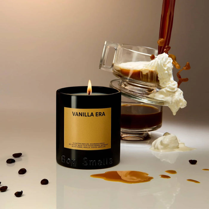 Boy Smells Vanilla Era scented 9 ounce Classics candle in black glass vessel, lit with espresso and whipped cream in the background.