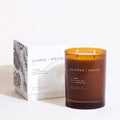 An amber glass jar candle labeled 'JUNIPER + SPRUCE' stands next to its white product box with botanical line art, on a clean white background.