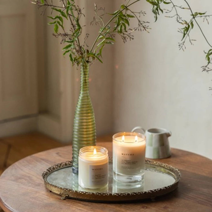 Two matcha candles on a decorative tray with a vase and branches in the background.