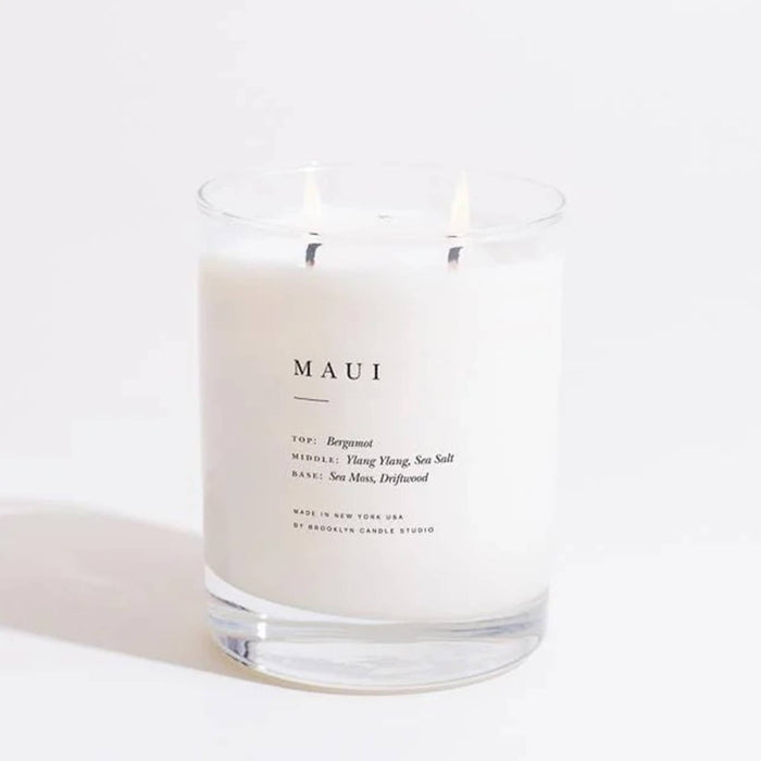 Maui scented candle in clear glass vessel with double wicks lit, on a white background.