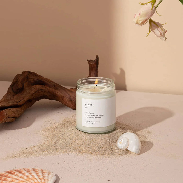 Jar candle labeled 'MAUI' with natural elements like driftwood and shells on a beige background.