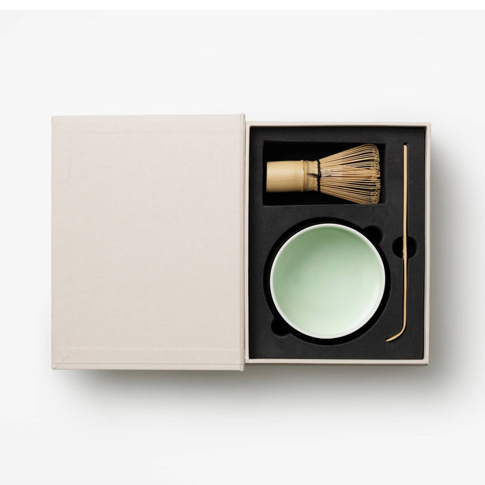 Matcha tool set with a green bowl and wooden whisk and spoon in a box on a white background.