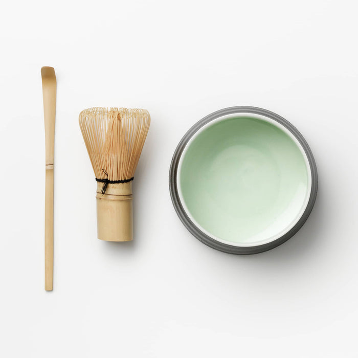 Matcha tool set with bowl, bamboo whisk, and bamboo spoon on a white background.