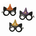 Three black cat-shaped party glasses with glittery witch hats on top, shown on a plain white background. The hats are orange, purple, and gold, with small white polka dots and gold buckle details.
