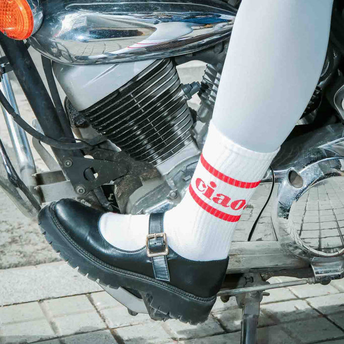 Person wearing a black shoe and white sock with red "ciao" text on a motorcycle.