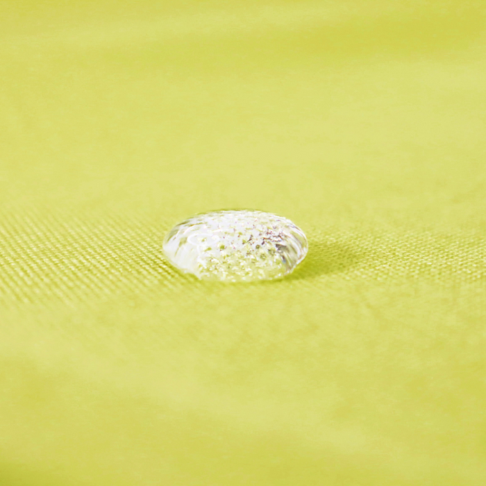 This waterproof canvas lite is a bright shade of green with yellow undertones. This specific photo is of a water droplet on the canvas.