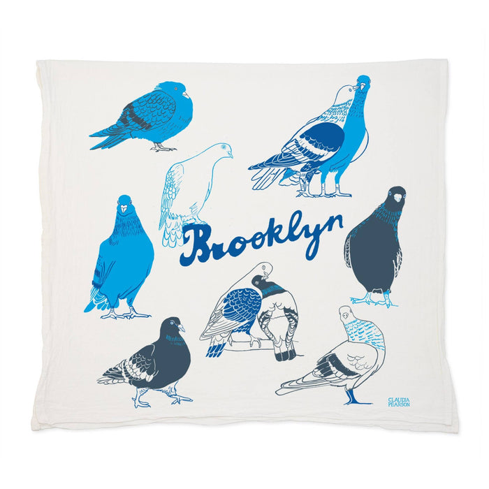 A square off-white flour sack cotton tea towel featuring a printed design of various pigeon illustrations in shades of blue and white, with the word 'Brooklyn' written across the center.