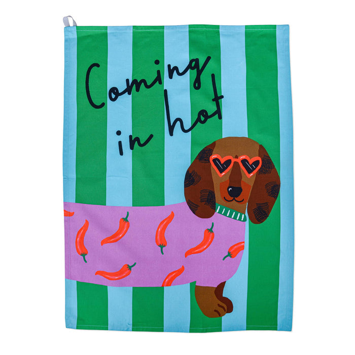 Green and blue striped cotton tea towel with a dachshund wearing a chili pepper sweater with "coming in hot" in black script lettering, flat on a white background.