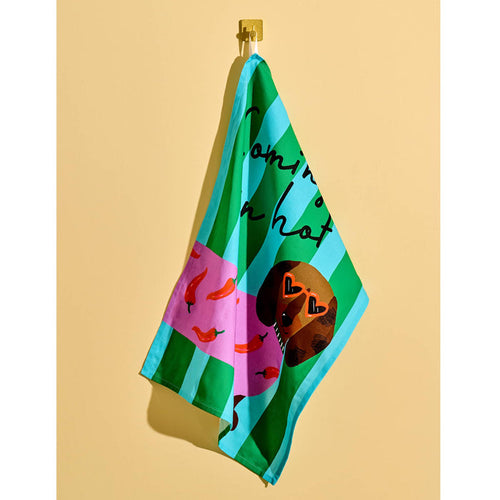 Green and blue striped cotton tea towel with a dachshund wearing a chili pepper sweater with "coming in hot" in black script lettering, hanging on a yellow background.