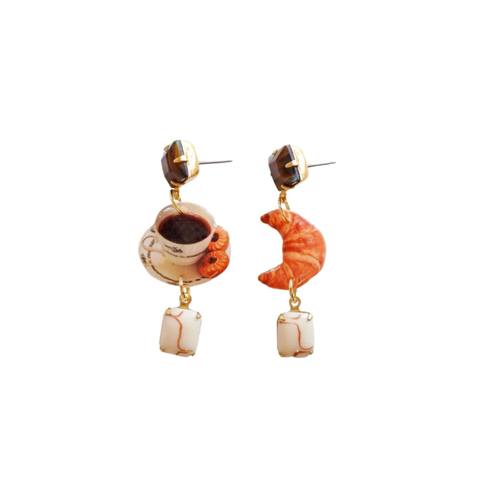 Pair of drop earrings with a coffee cup and saucer and a croissant with vintage components, on a white background.