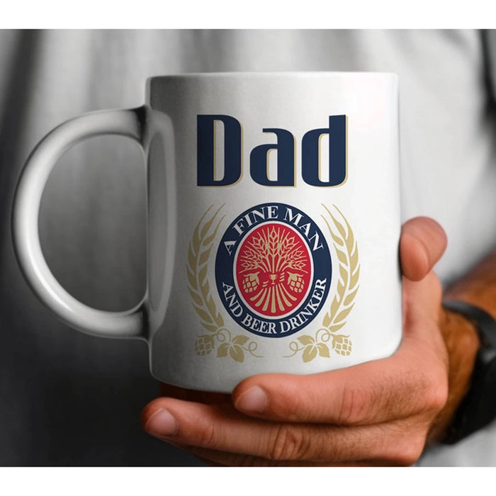 White mug with 'Dad' and a beer logo parody held by a person.